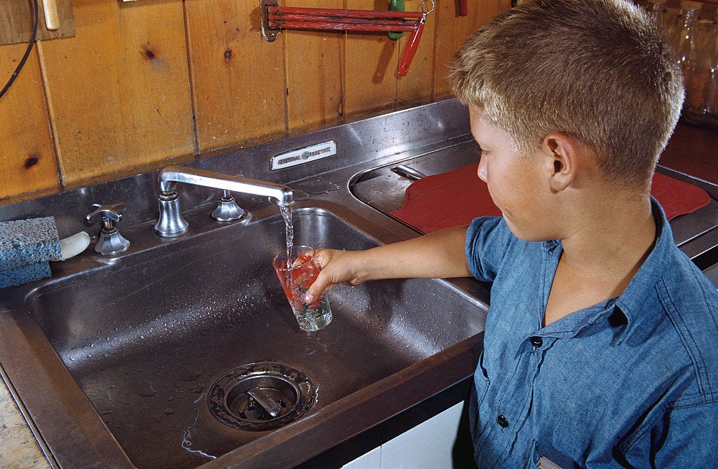 A boy is filling a glass with water in a kitchen sink. A boy is filling a glass with water in a kitchen sink.