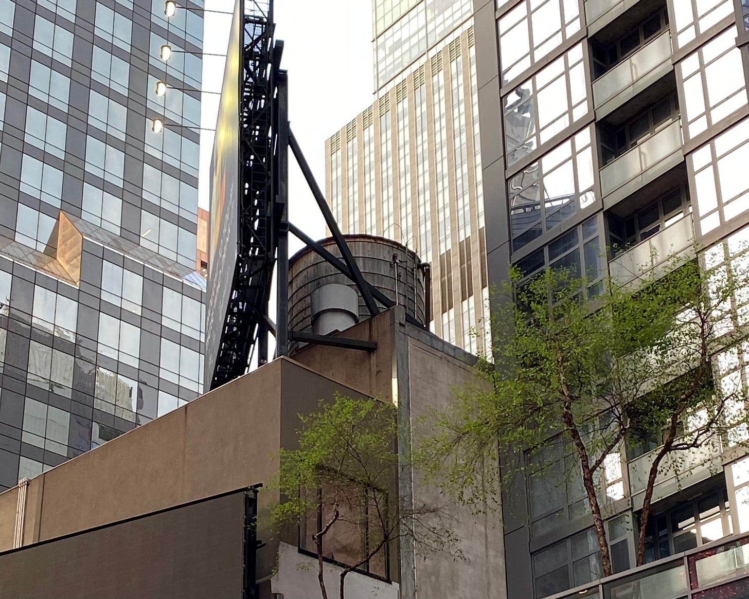 A water tower concealed by a billboard viewed from the side. On either side are modern buildings of glass and metal.