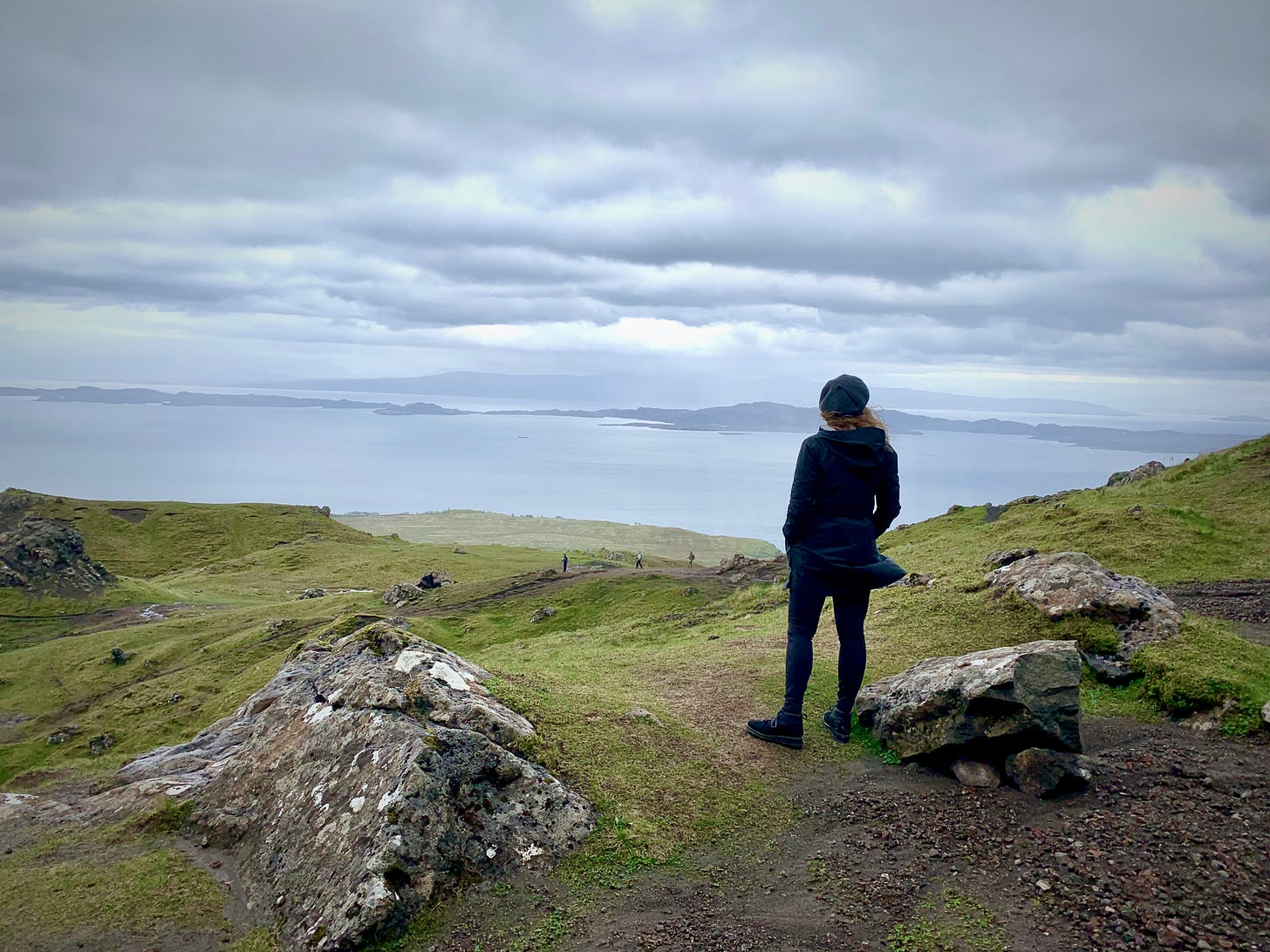 Karista standing at the top of The Old Man of Storr in the Scottish Highlands and looking over the view of the water below