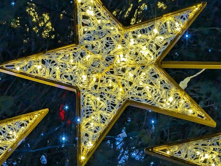 Three lighted stars on a pole in front of a tree