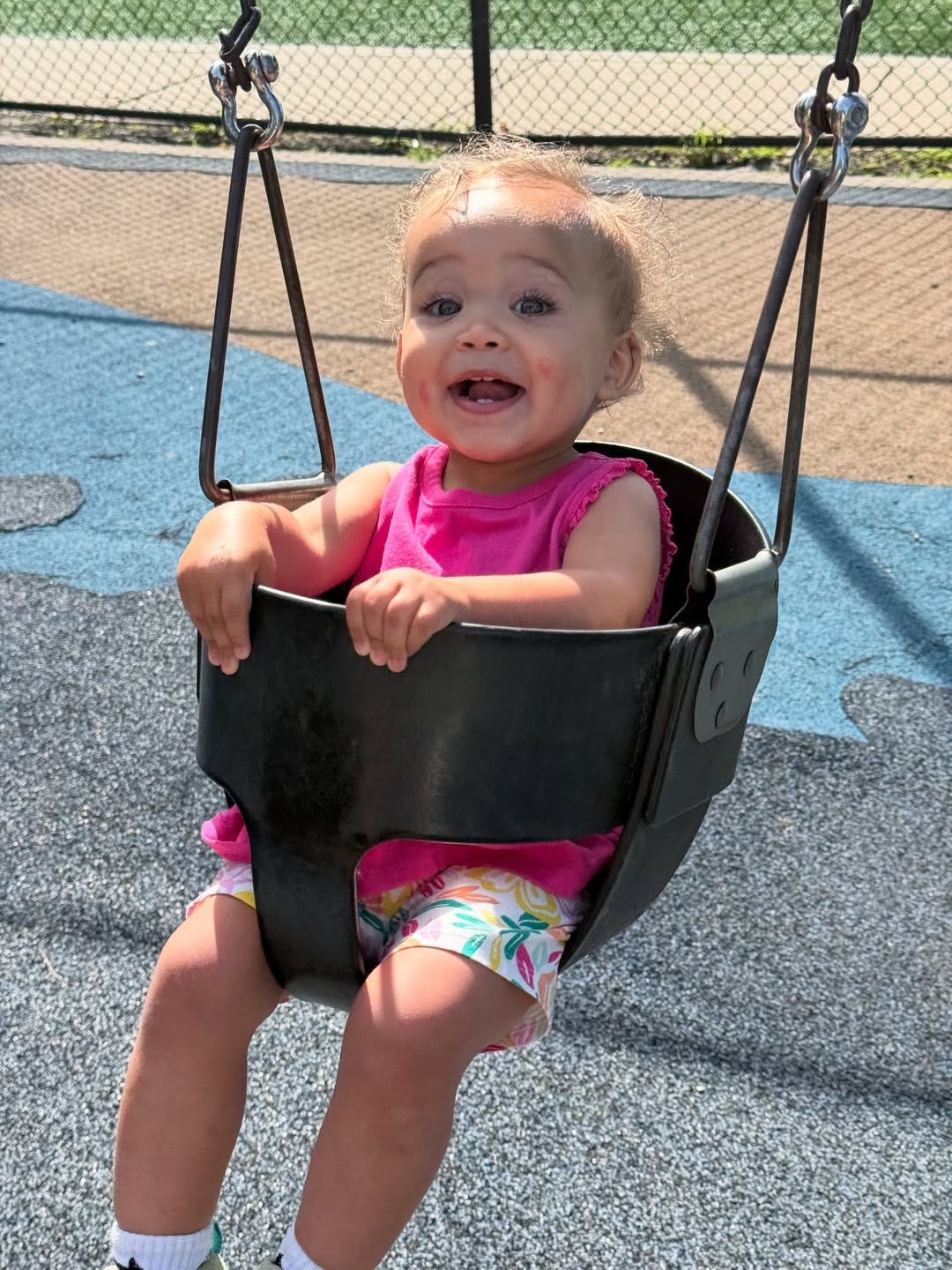 two year old girl in a pink t shirt sitting in an outside swing