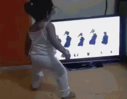a little girl is dancing in front of a television screen