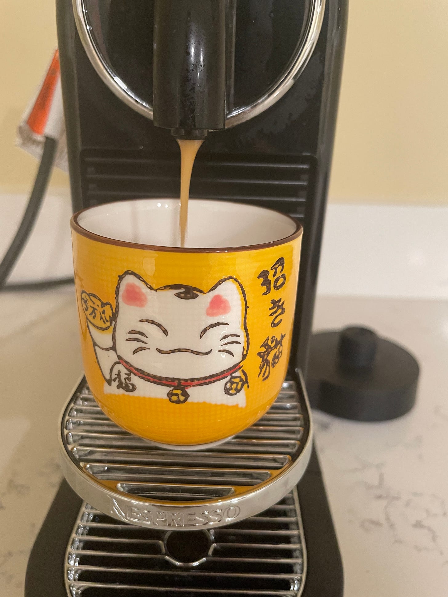 espresso pouring into cute, yellow cup with lucky cat
