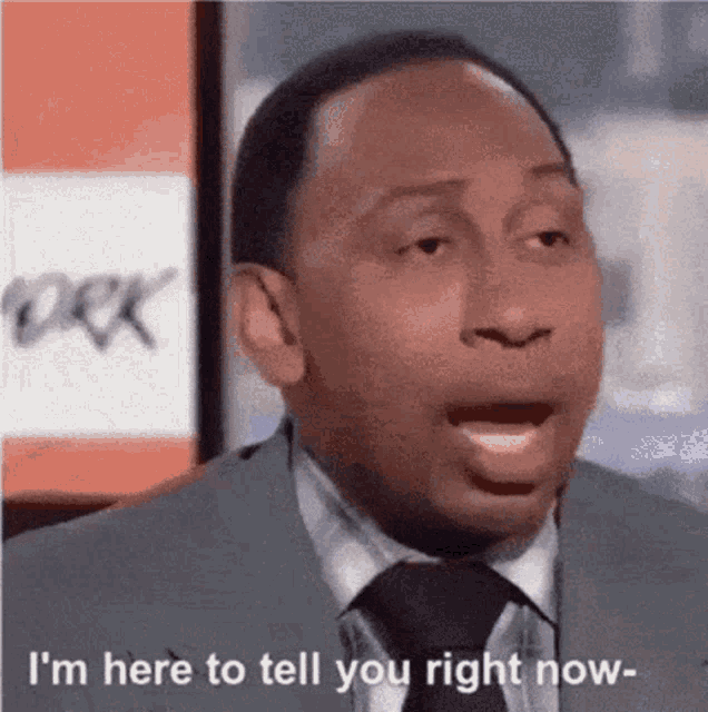 a man in a suit and tie is standing in front of a sign that says i 'm here to tell you right now .