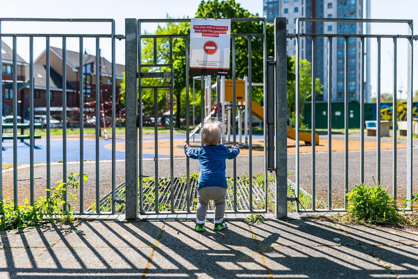A toddler in front of a locked playground during the Covid pandemic