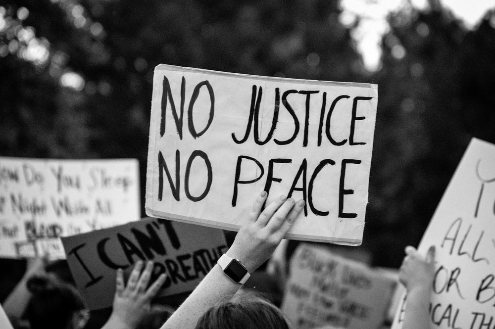 a peaceful black lives matter protest, holding a sign that says "no justice no peace" in downtown within the streets