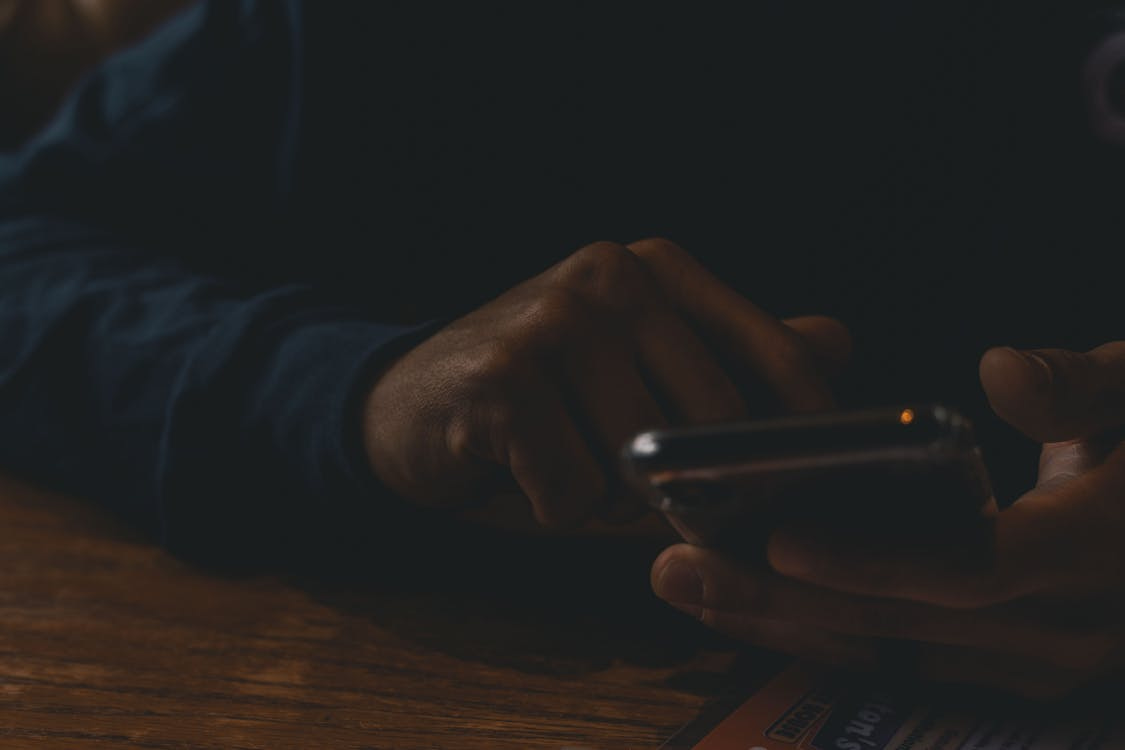 Free A close-up view of hands interacting with a smartphone in a dim indoor setting, highlighting technology use. Stock Photo