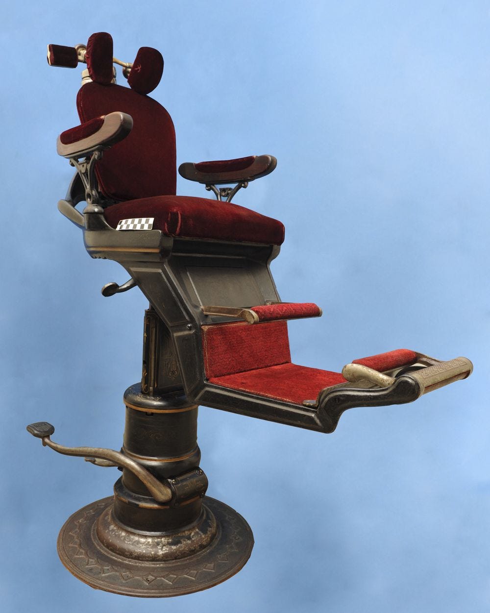 a photo of a late 1800s dentist chair with red velvet upholstery and a metal base a photo of a late 1800s dentist chair with red velvet upholstery and a metal base