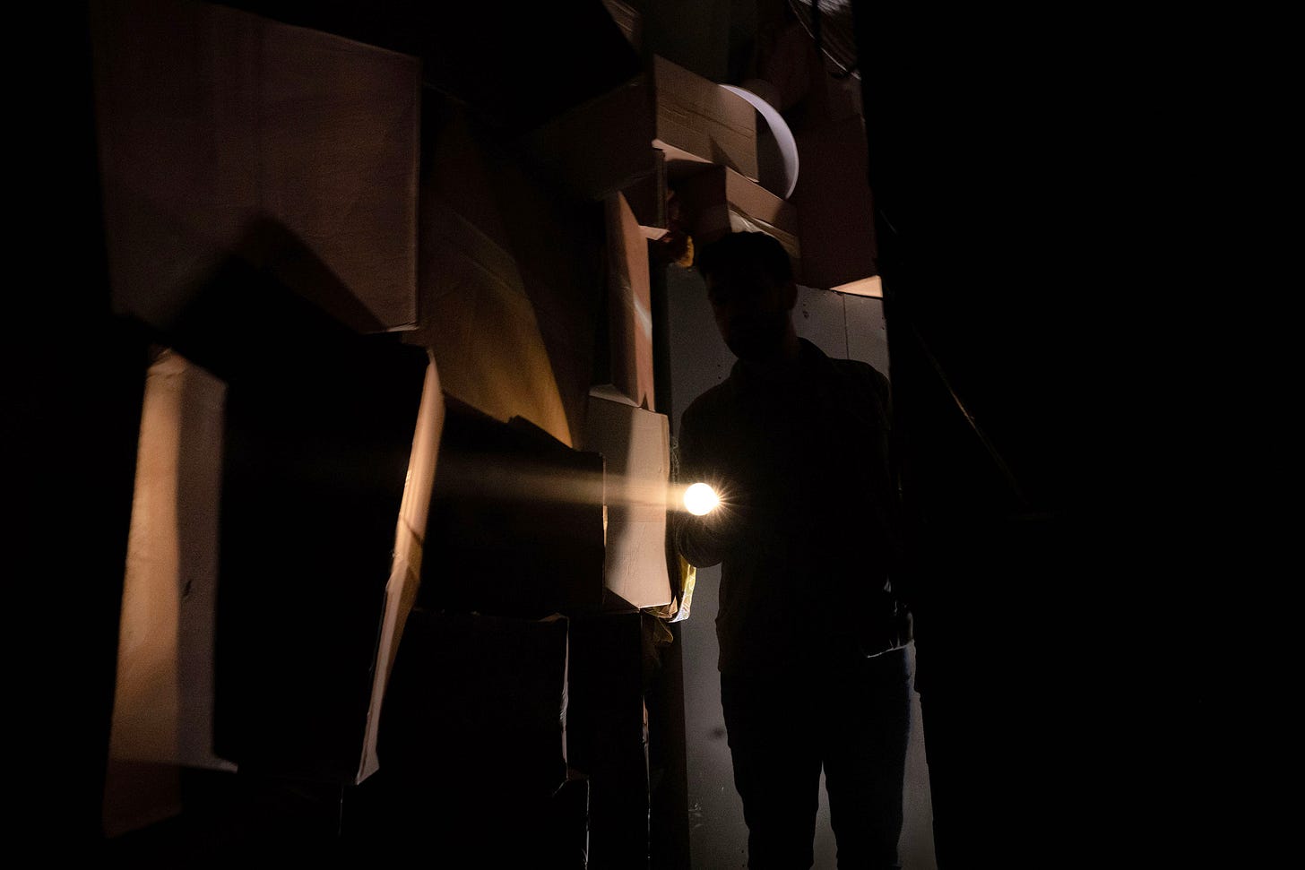 A person shines a torch through a corridor of boxes