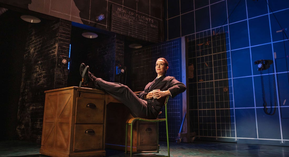 A woman on stage with her feet up on a desk