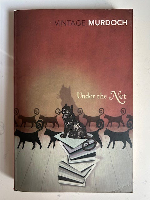 A red background with several black cats walking from right to left. In the center, a cat sits on a stack of books