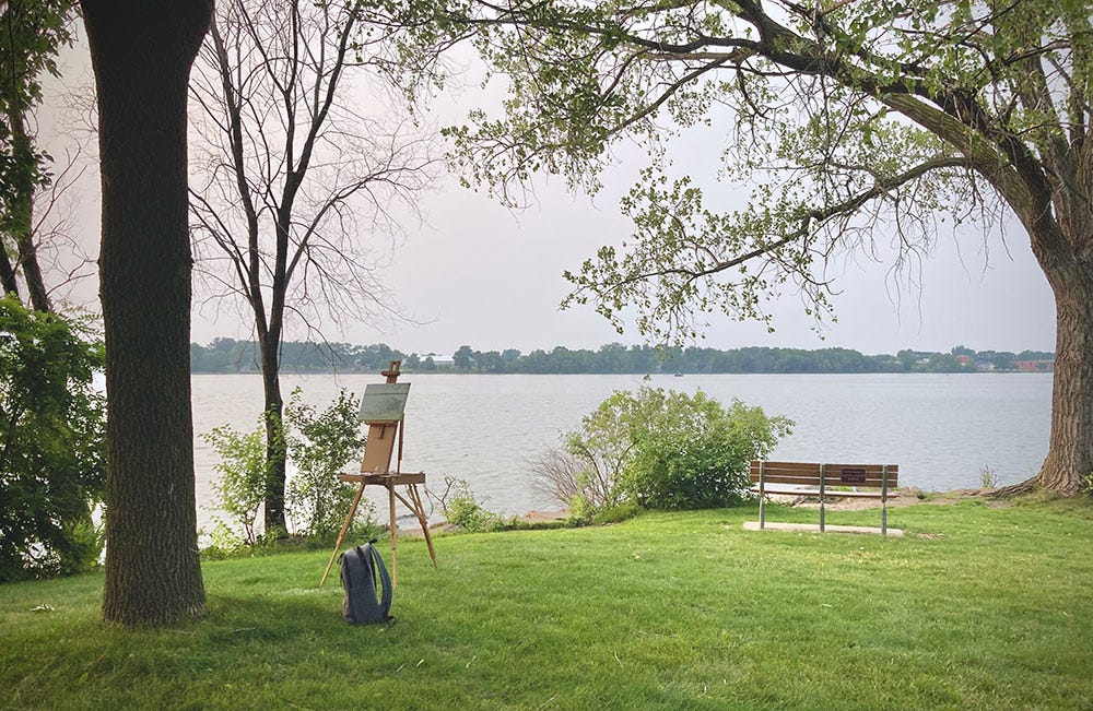 An easel set up next to a river beneath a tree