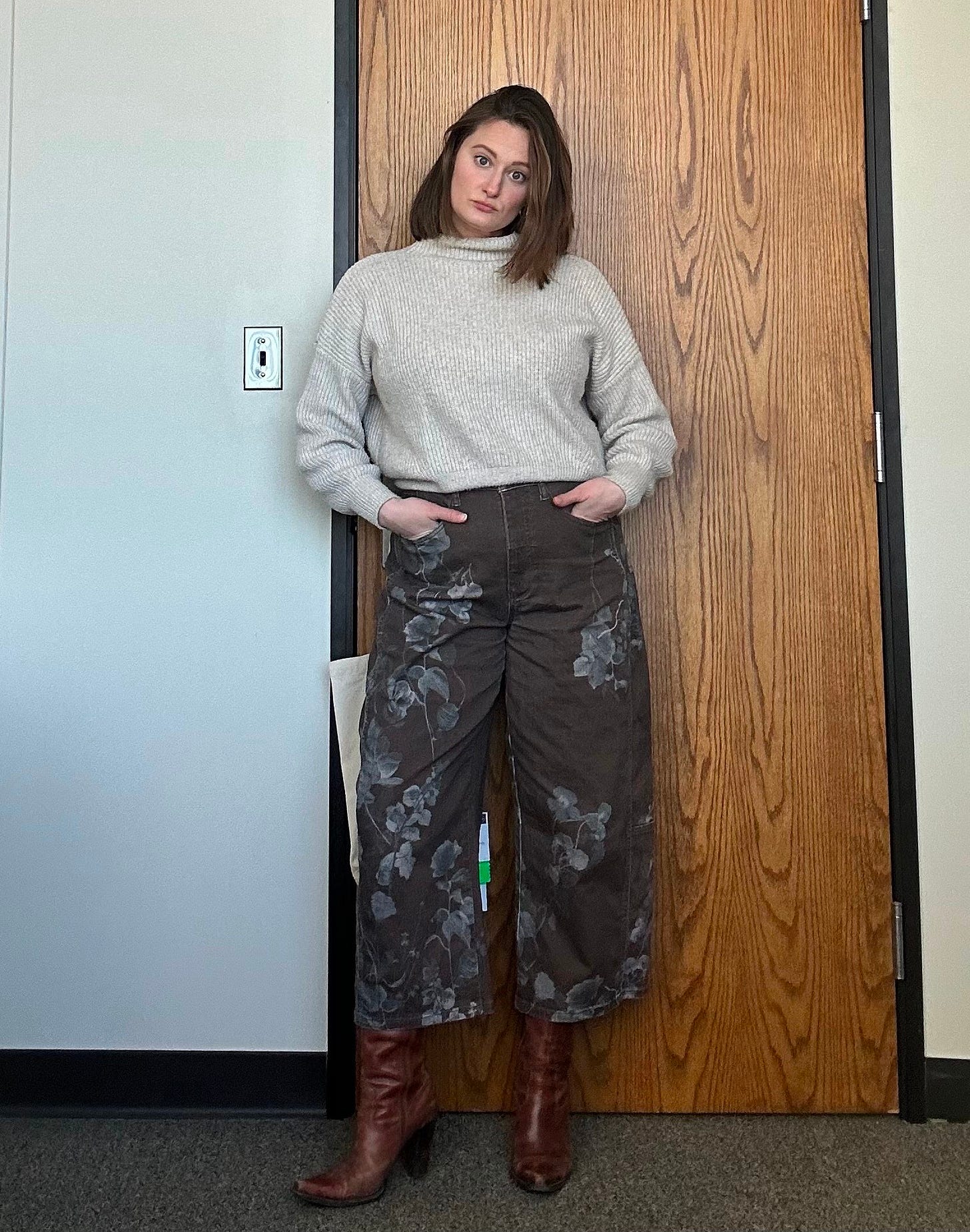 Brunette woman standing in office with brown barrel jeans on and a tan sweater Brunette woman standing in office with brown barrel jeans on and a tan sweater