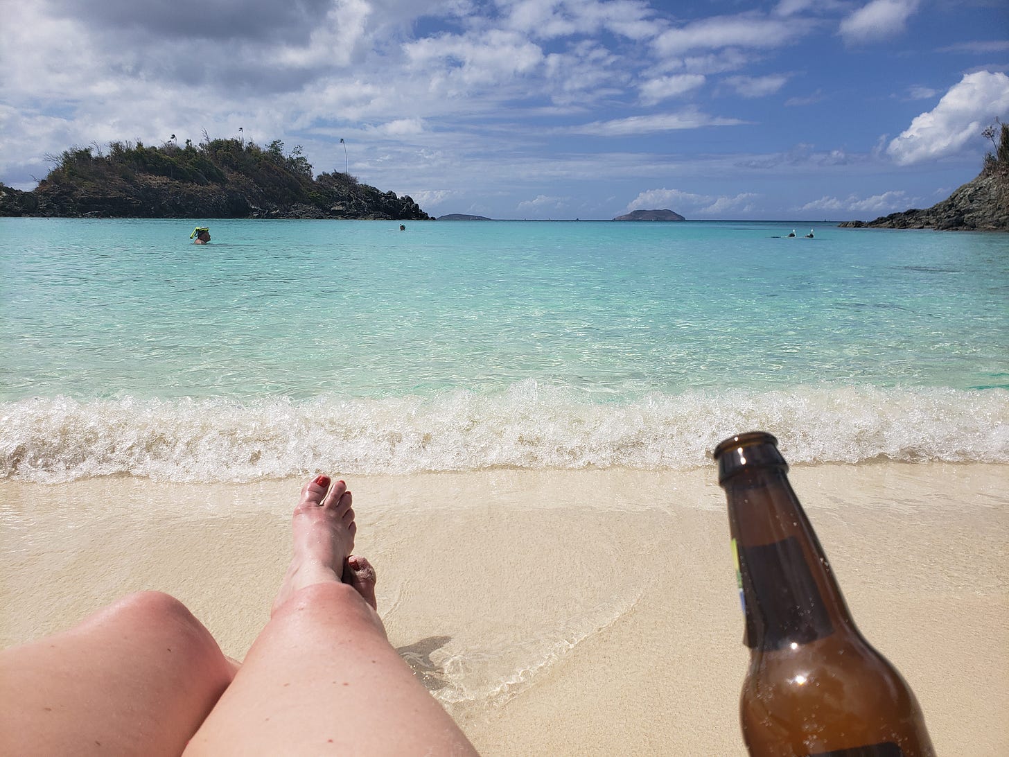 woman's legs on beach with Carribean blue water and a beer bottle