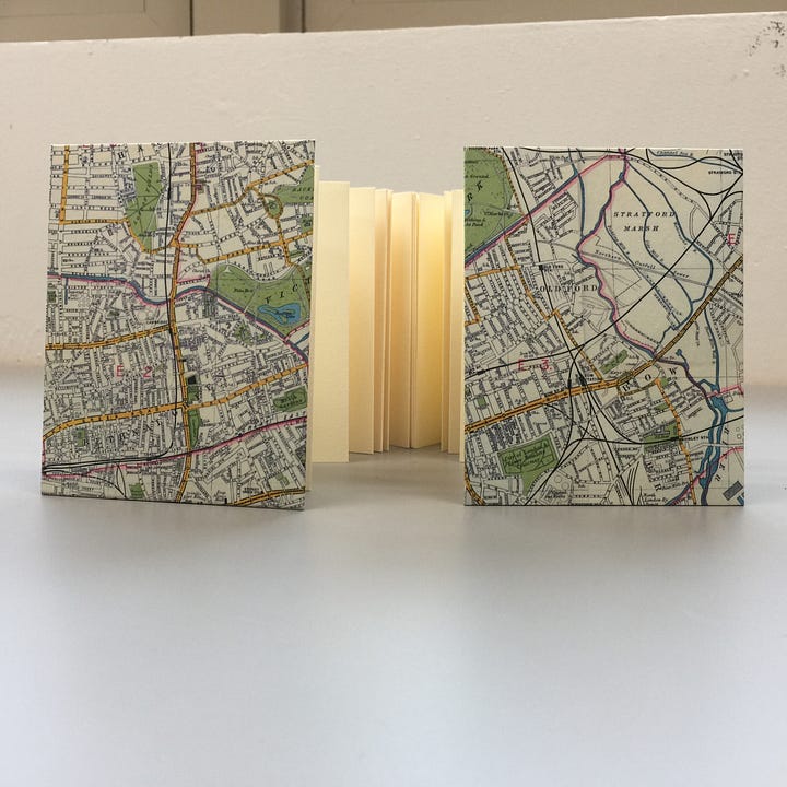 An accordion binding, first image: back and front hard cover, wrapped in map paper, a peak of cream paper folded in between. second image: an overhead view of the folded pages shaped like a U.