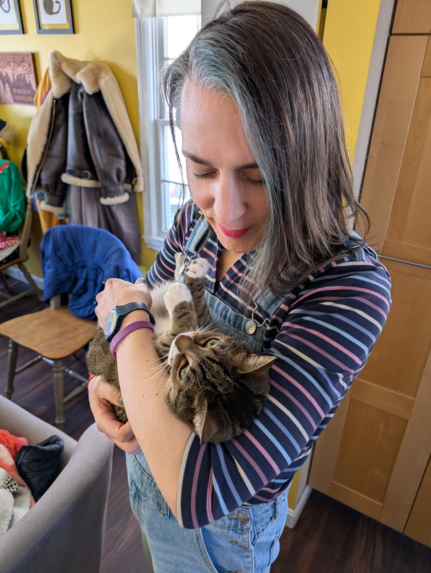 A non-binary human cradles a cat, who contently makes air biscuits A non-binary human cradles a cat, who contently makes air biscuits