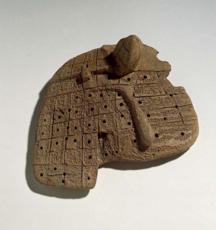 Modelo de argila do fígado de uma ovelha. Uma tabuinha de coloração marrom, cheia de inscrições, dividida em quadrados com vários furinhos.