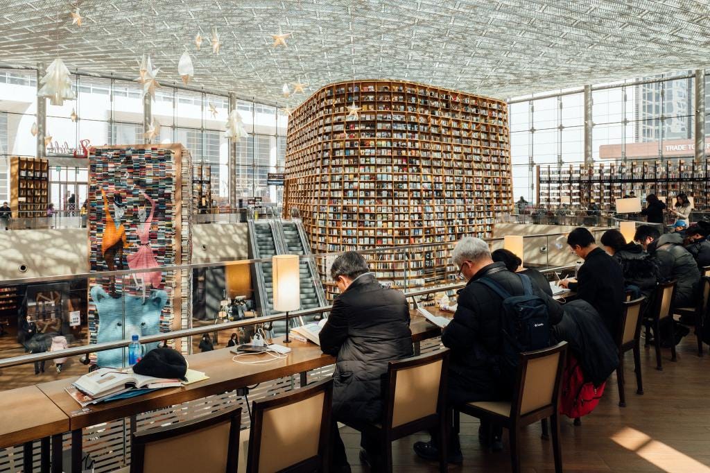 The picture depicts a group of customers seated in a reading area in the library, studying materials from the collection.