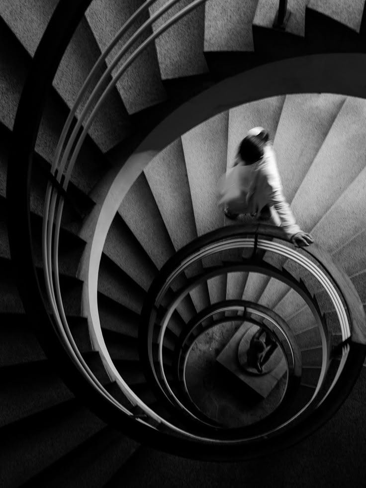 This may contain: black and white photograph of man walking down spiral staircase