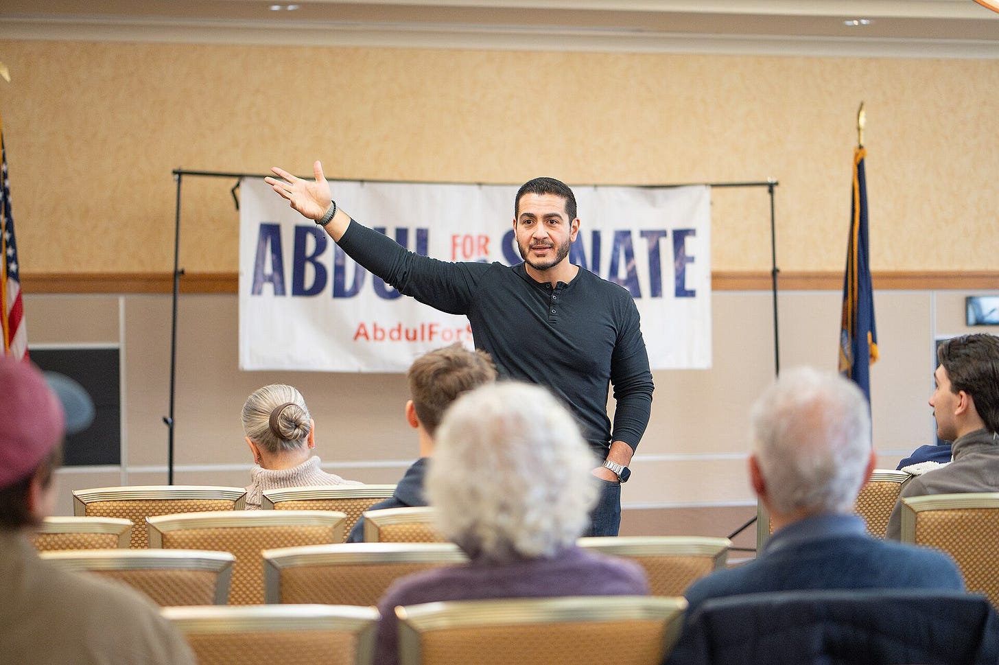 Abdul El-Sayed gesturing in front of a small crowd; behind him is an abdul el-sayed for senate banner Abdul El-Sayed gesturing in front of a small crowd; behind him is an abdul el-sayed for senate banner