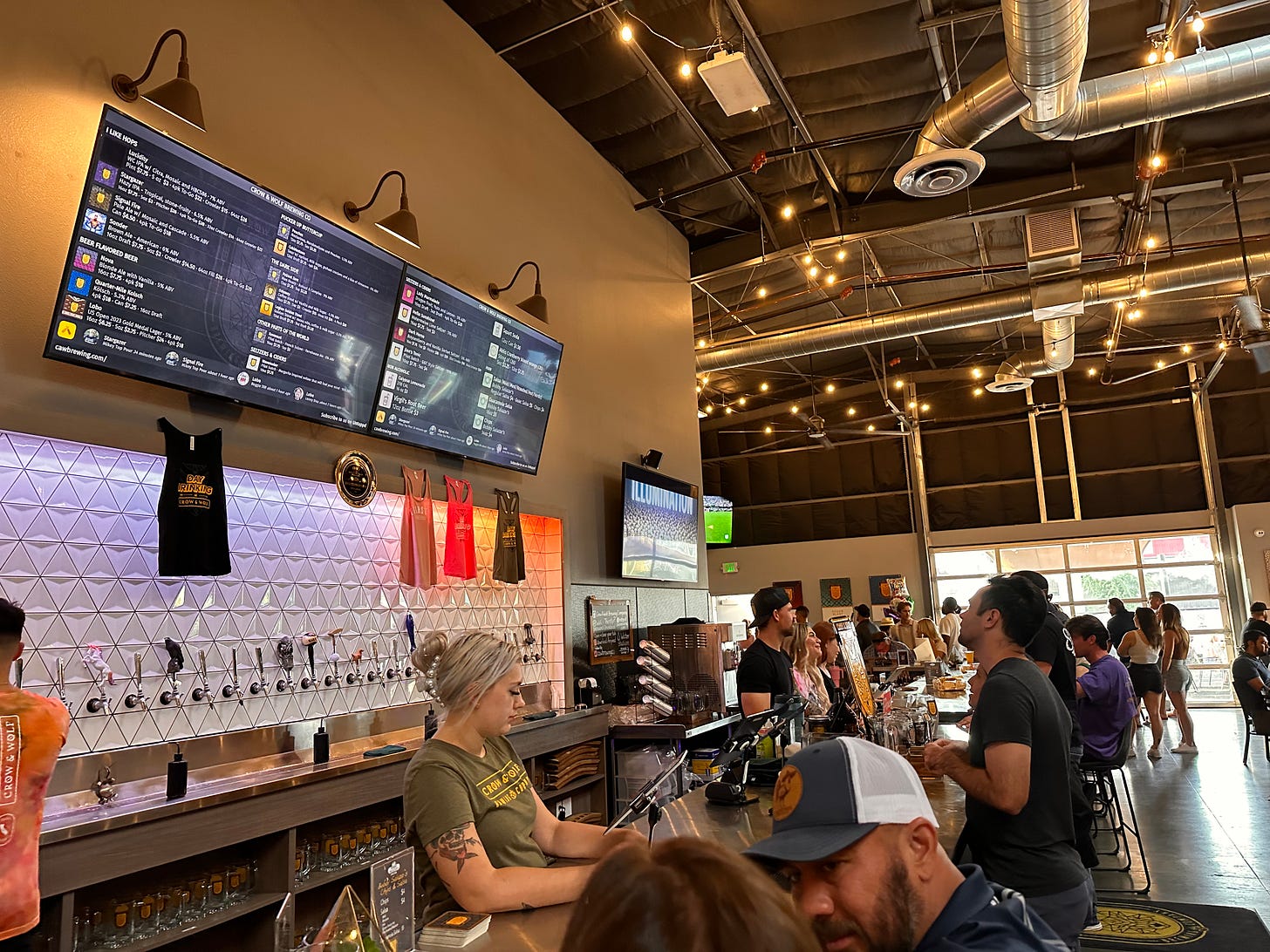 Busy taproom of Crow & Wolf Brewing with a bar and an Untappd board above the taps