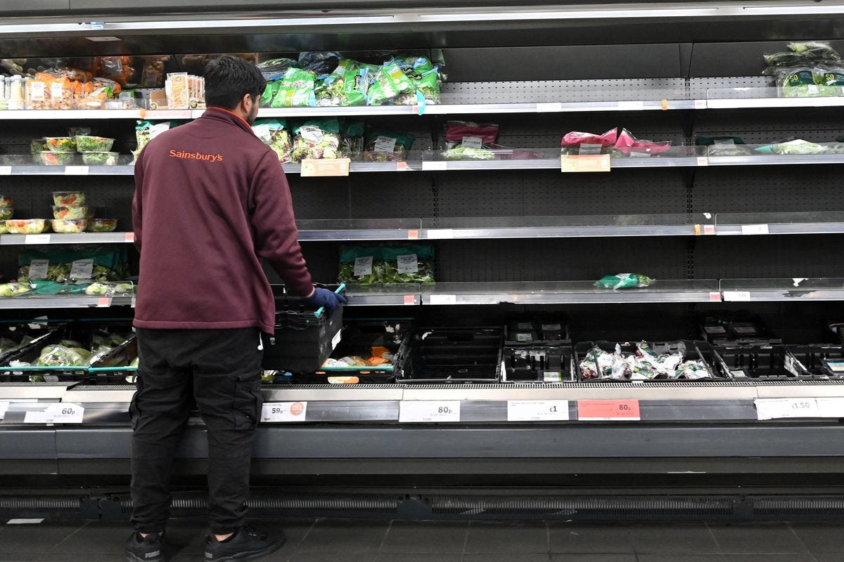 Empty fresh produce shelves at Sainsbury’s are tended to by a staff member