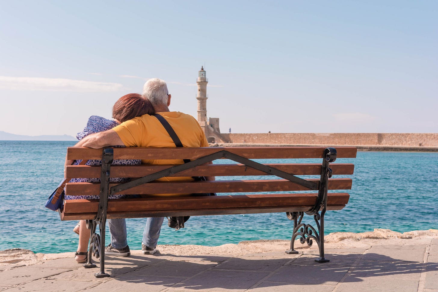 An elderly couple enjoys a peaceful moment by the sea, seated on a bench with a lighthouse in view for Kay Fabella's Edgewalkers Collective essay on When You Can't Reach Family Members Overnight from Abroad An elderly couple enjoys a peaceful moment by the sea, seated on a bench with a lighthouse in view for Kay Fabella's Edgewalkers Collective essay on When You Can't Reach Family Members Overnight from Abroad