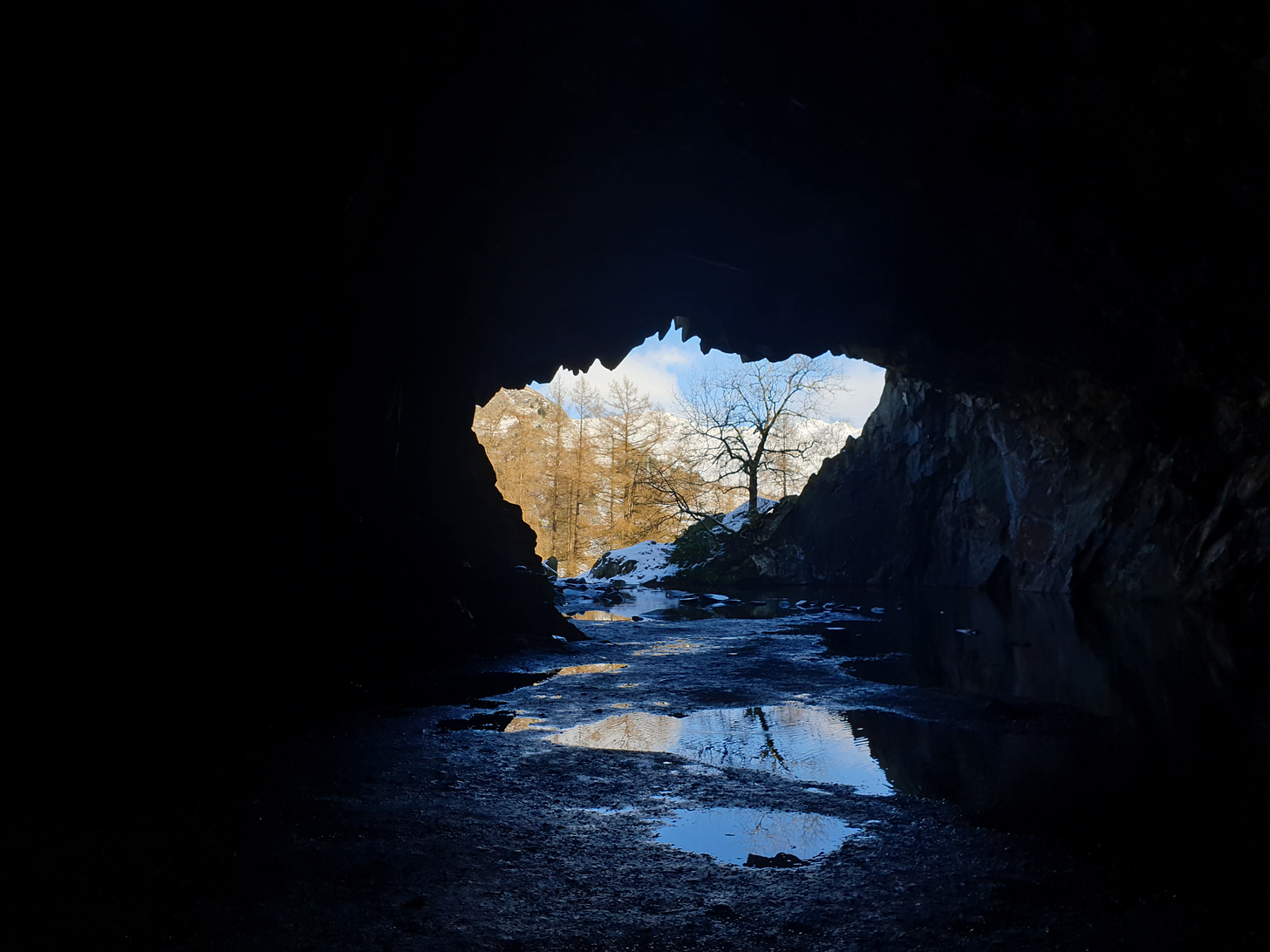Looking out from a cave, the opening to a winter landscape appears small in comparison to the blackness surrounding it