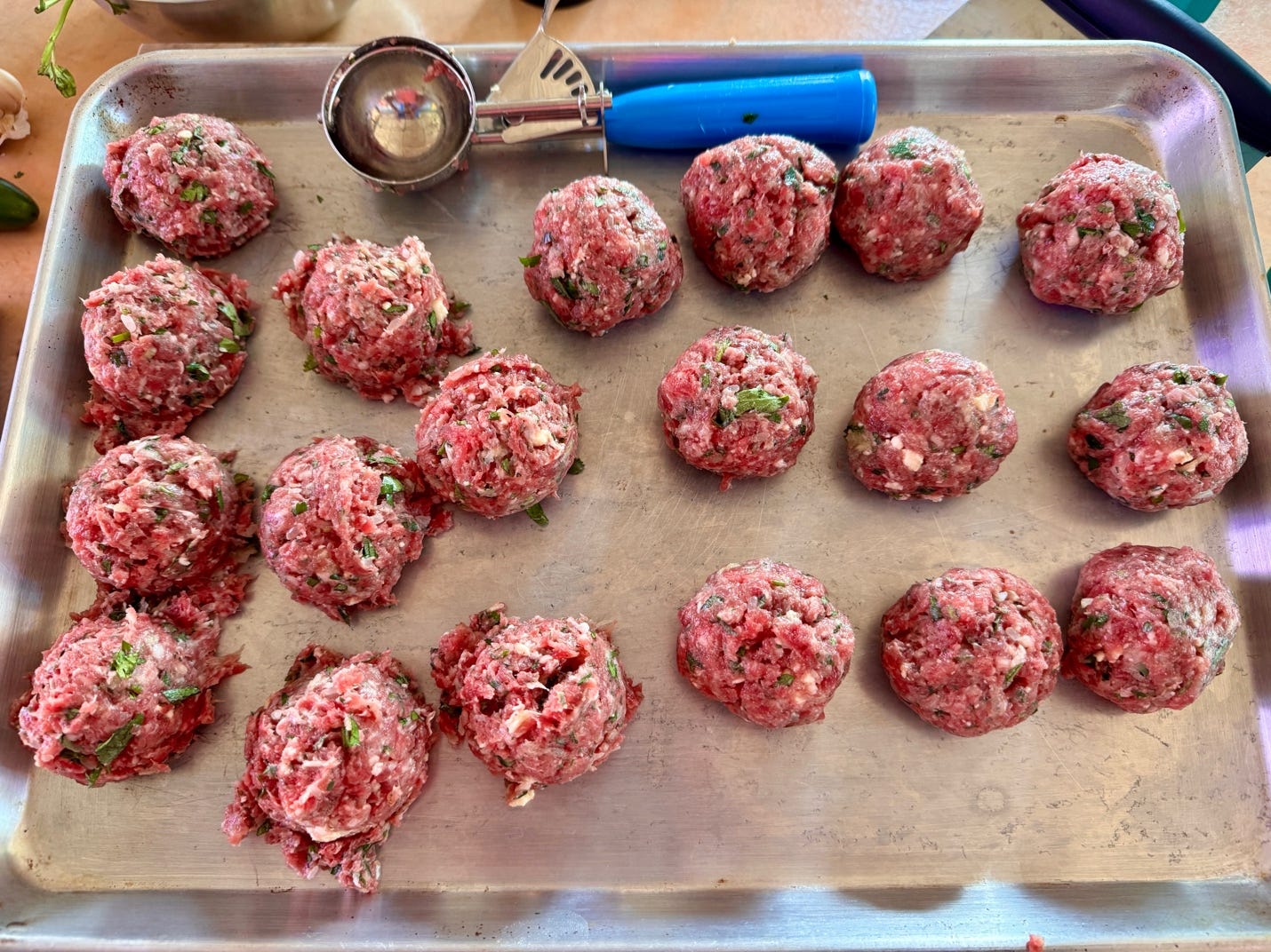 Using an ice cream scoop to portion the ground beef mixture evenly before shaping it by hand into tight, round meatballs.
