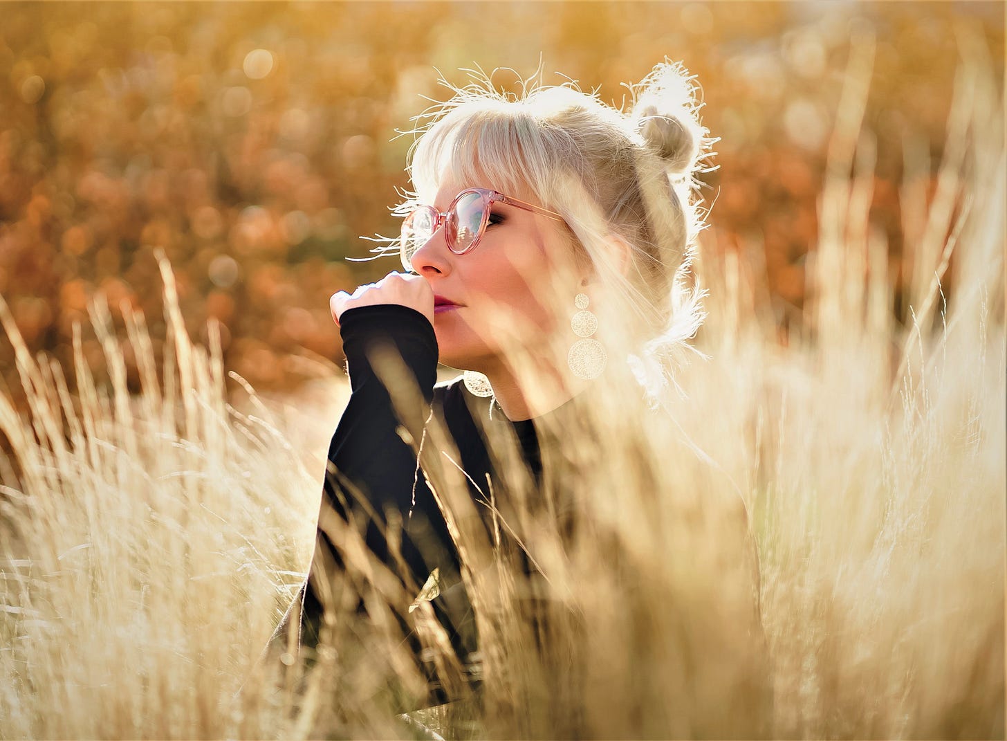 woman with blonde hair wearing glasses and black top sitting in wheat field