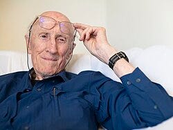 close-up of Stewart Brand wearing a dark blue shirt, holding his glasses up slightly above his eyes, smiling and looking left of camera close-up of Stewart Brand wearing a dark blue shirt, holding his glasses up slightly above his eyes, smiling and looking left of camera