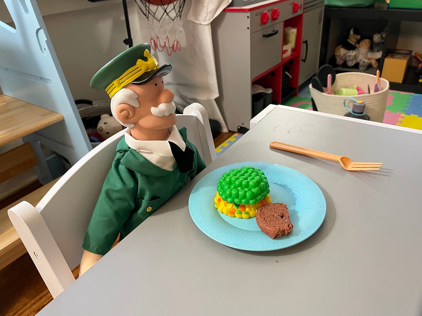 Sarge doll in green uniform with white hair and white mustache, propped at a child's table with fake and real food in front of him.