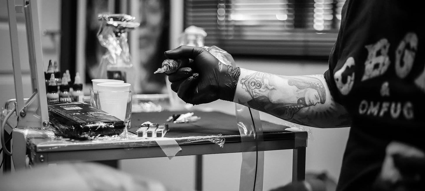 A man with tattoos on his arm holding a tattoo gun. A man with tattoos on his arm holding a tattoo gun.