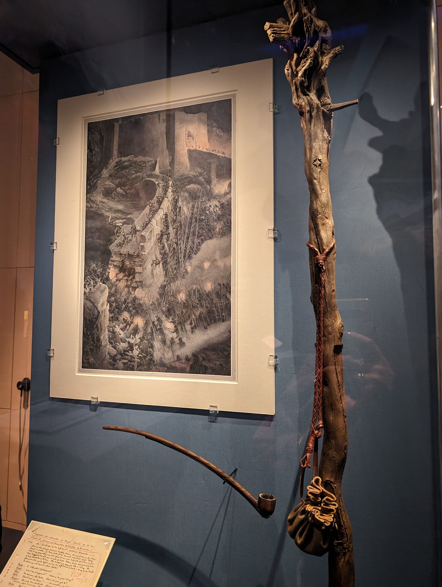 An original Alan Lee watercolour of the breach of the wall at Helm's Deep from The Two Towers, next to Gandalf's staff and pipe from the movies.