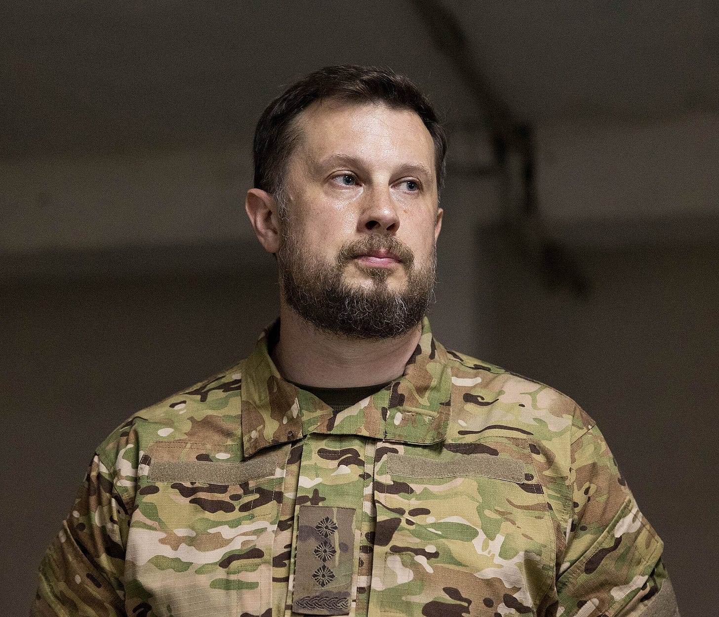 Portrait of Andrii Biletskyi, a bearded man in a multicam camouflage uniform, looking to his right. Portrait of Andrii Biletskyi, a bearded man in a multicam camouflage uniform, looking to his right.