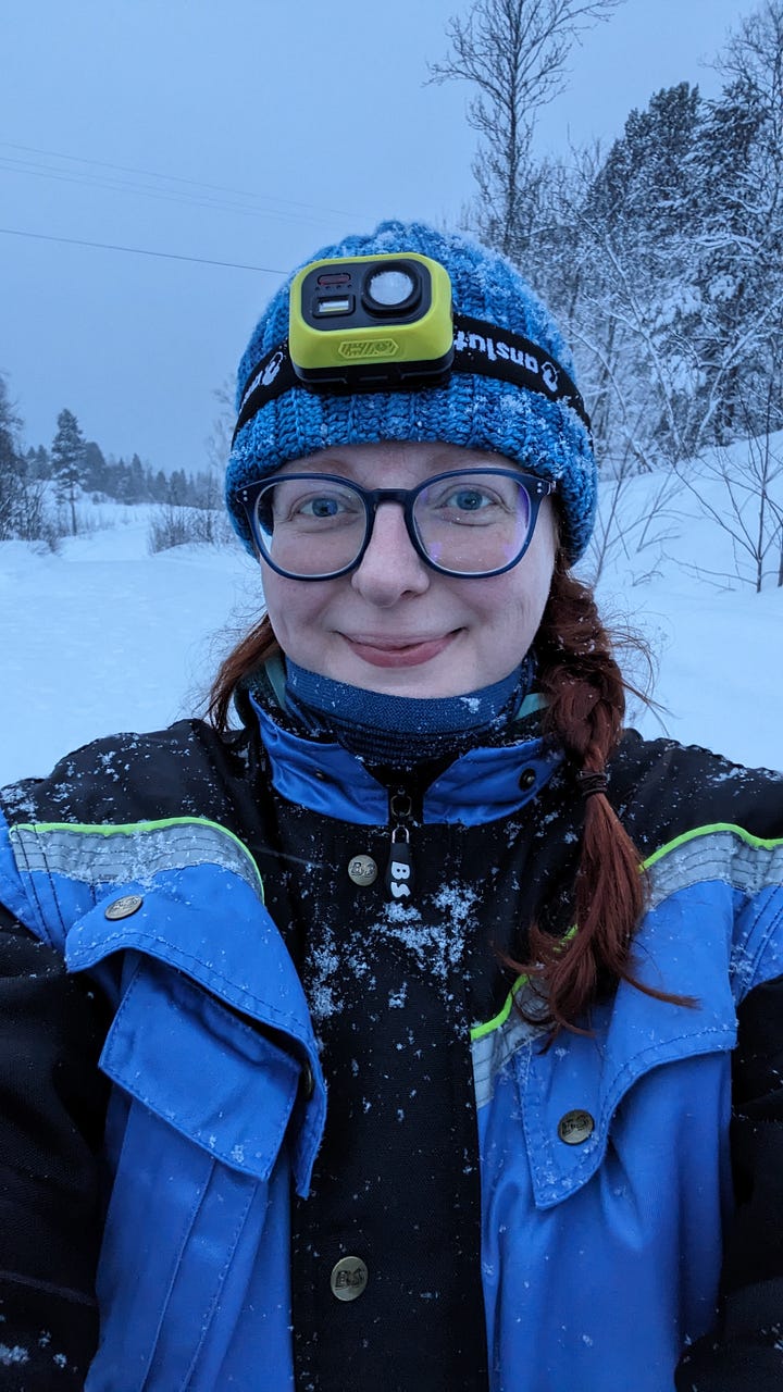 Images showing a red-haired woman in a blue snowsuit crouching and feeding white and brown reindeer. One shows a white Lavvu tent, it's internal fire glowing through the entrance.