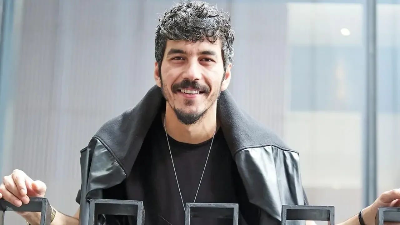 Mert Doğan gülümseyen pozunda — siyah deri yelek ve kolye ile set fotoğrafı