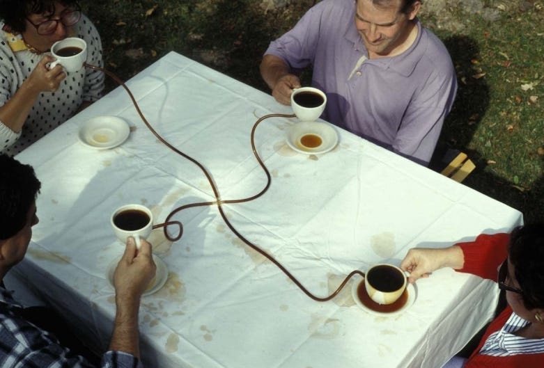 In Allan Wexler's work titled "Coffee Seeks its Own Level," four people sit around a table drinking from coffee cups that are connected by clear rubber tubing. Coffee spills and modest overflows are evident around the saucers of each drinker. In Allan Wexler's work titled "Coffee Seeks its Own Level," four people sit around a table drinking from coffee cups that are connected by clear rubber tubing. Coffee spills and modest overflows are evident around the saucers of each drinker.