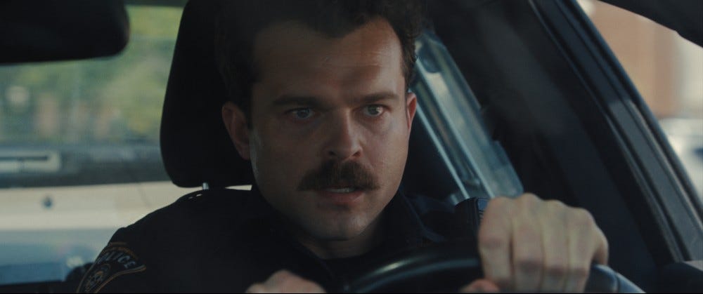 Alden Ehrenreich as a police officer in Weapons, behind the wheel of his car.