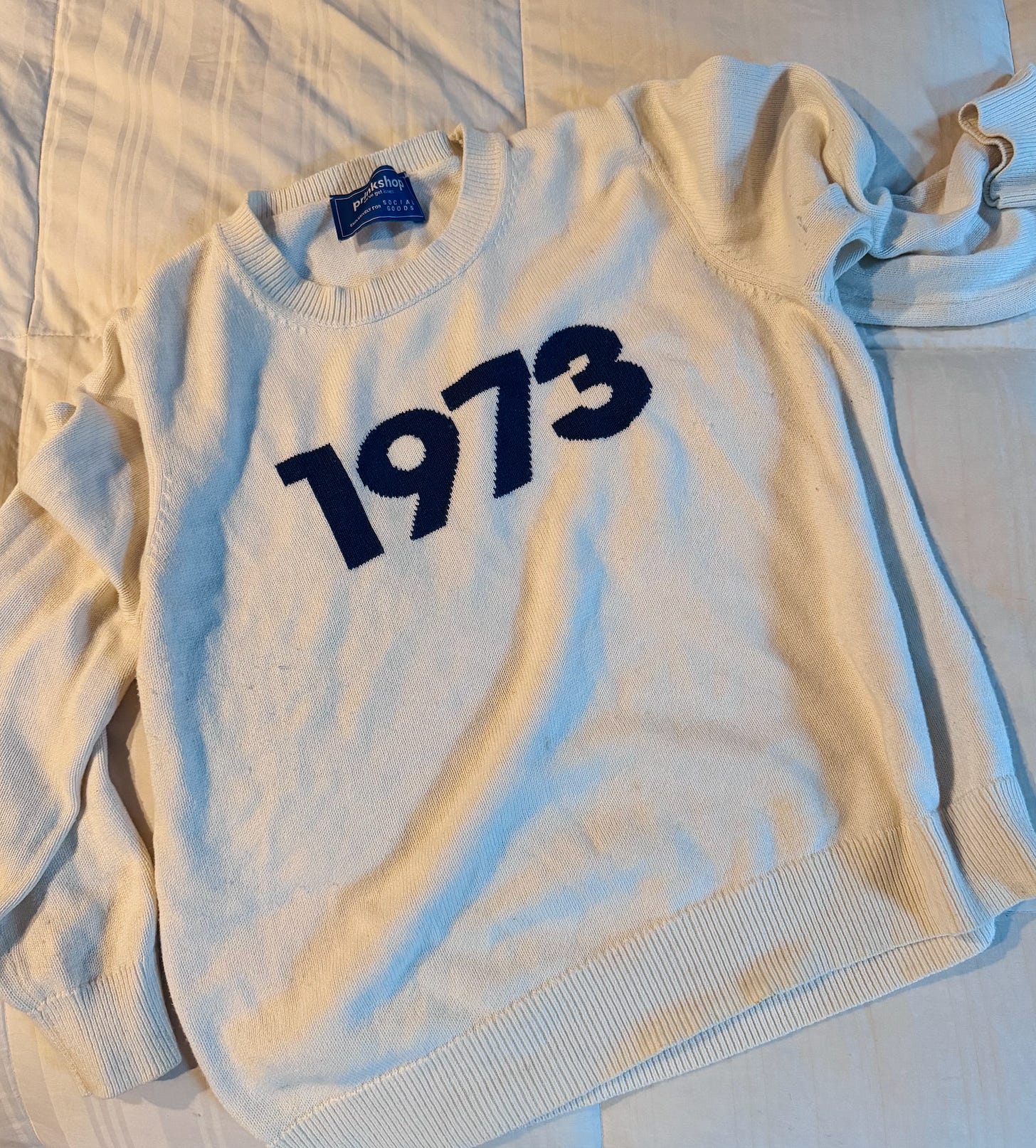 A white knit sweater with navy blue text across the chest that reads “1973.”