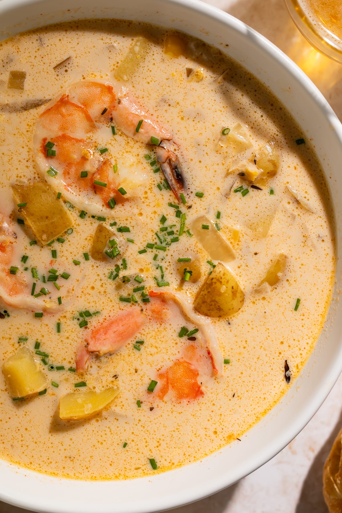 Bowl of creamy chowder with shrimp and potatoes, garnished with snipped chives, surrounded by crusty baguette and glasses of beer