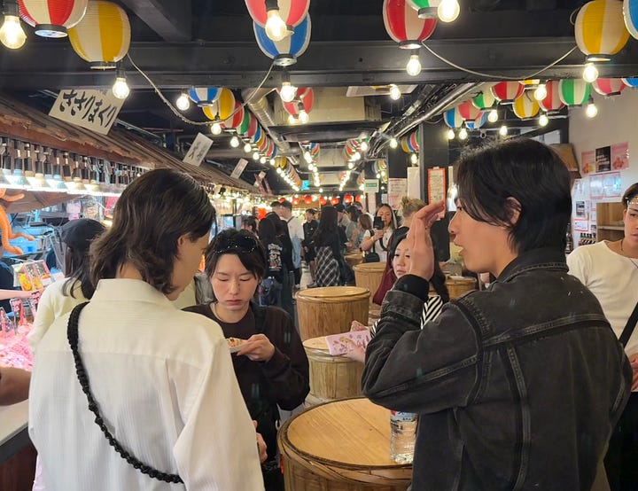 Left: the covered Nishiki market arcade in Kyoto, lined with food stalls. Right: two women sampling food at a market vendor.