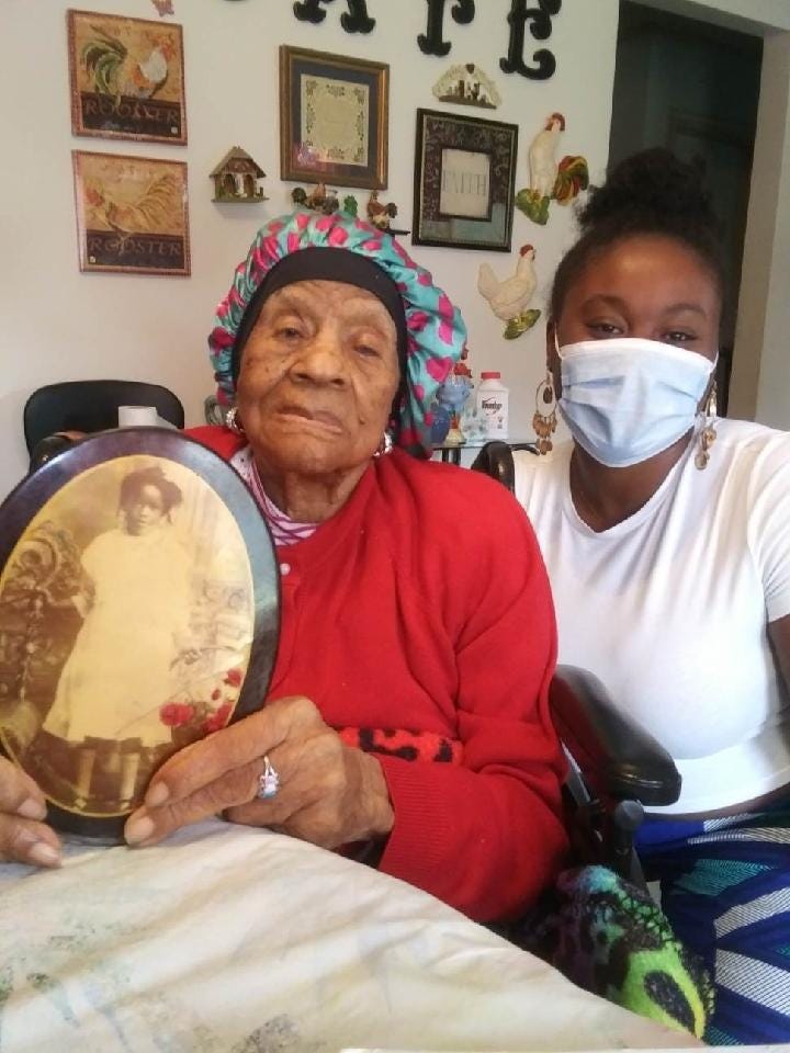 Miss oden seated holding a childhood photo of herself with alexis beside her in a mask and white tshirt