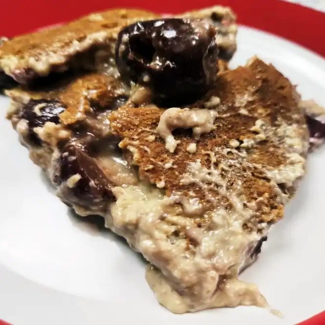 Plant Based Dark Cherry Clafoutis on a red rimmed white plate with a cherry on top.