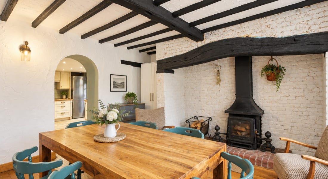 A dining room with white walls, dark wooden beams, and a wooden table with blue chairs A dining room with white walls, dark wooden beams, and a wooden table with blue chairs