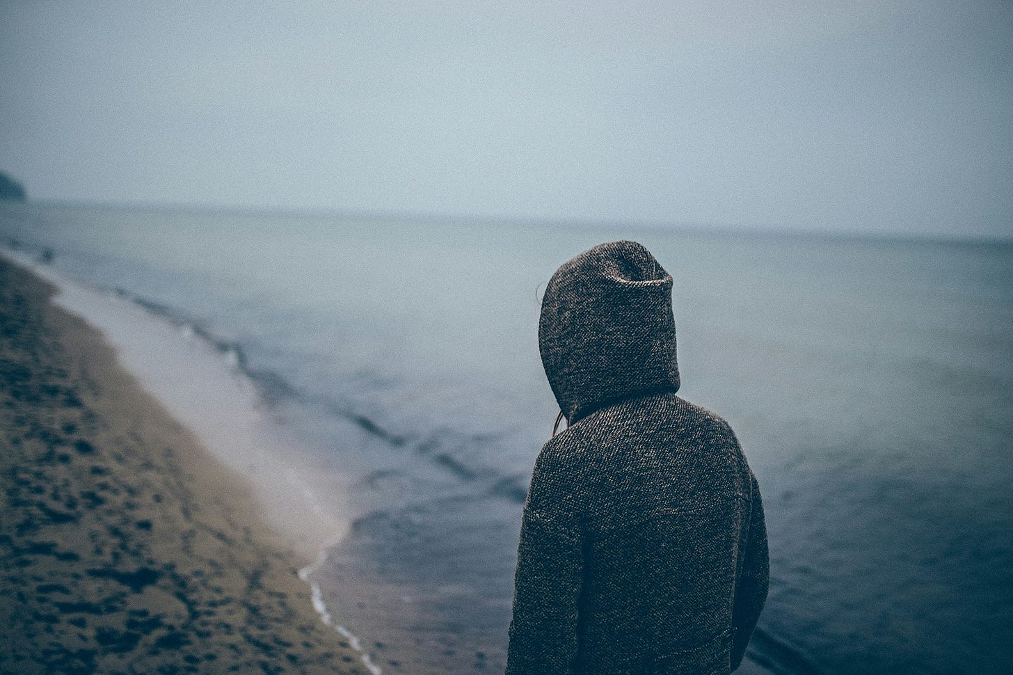 Photo of a person's back. They are in a hoody looking at the ocean. Photo by p - via Unsplash.