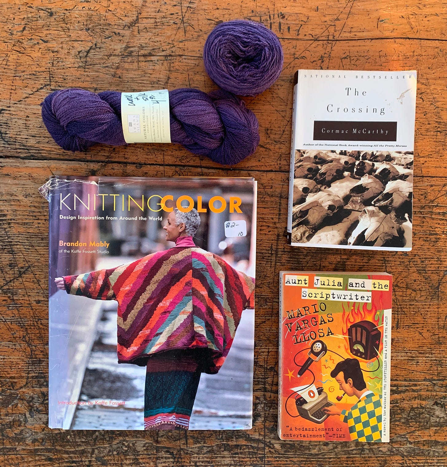 three books, a hank of yarn, and a cake of yarn on a wooden table