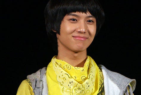 Taemin stands in casual late-2000s streetwear, wearing a layered graphic T-shirt, skinny jeans, and sneakers. His hair is cut in the rounded style associated with SHINee's debut era. 