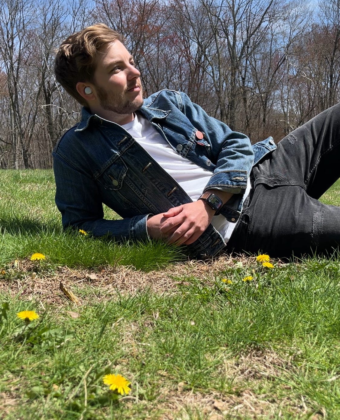 Jackson Bird reclining on some grass strewn with yellow dandelions. He's looking off in the distance.