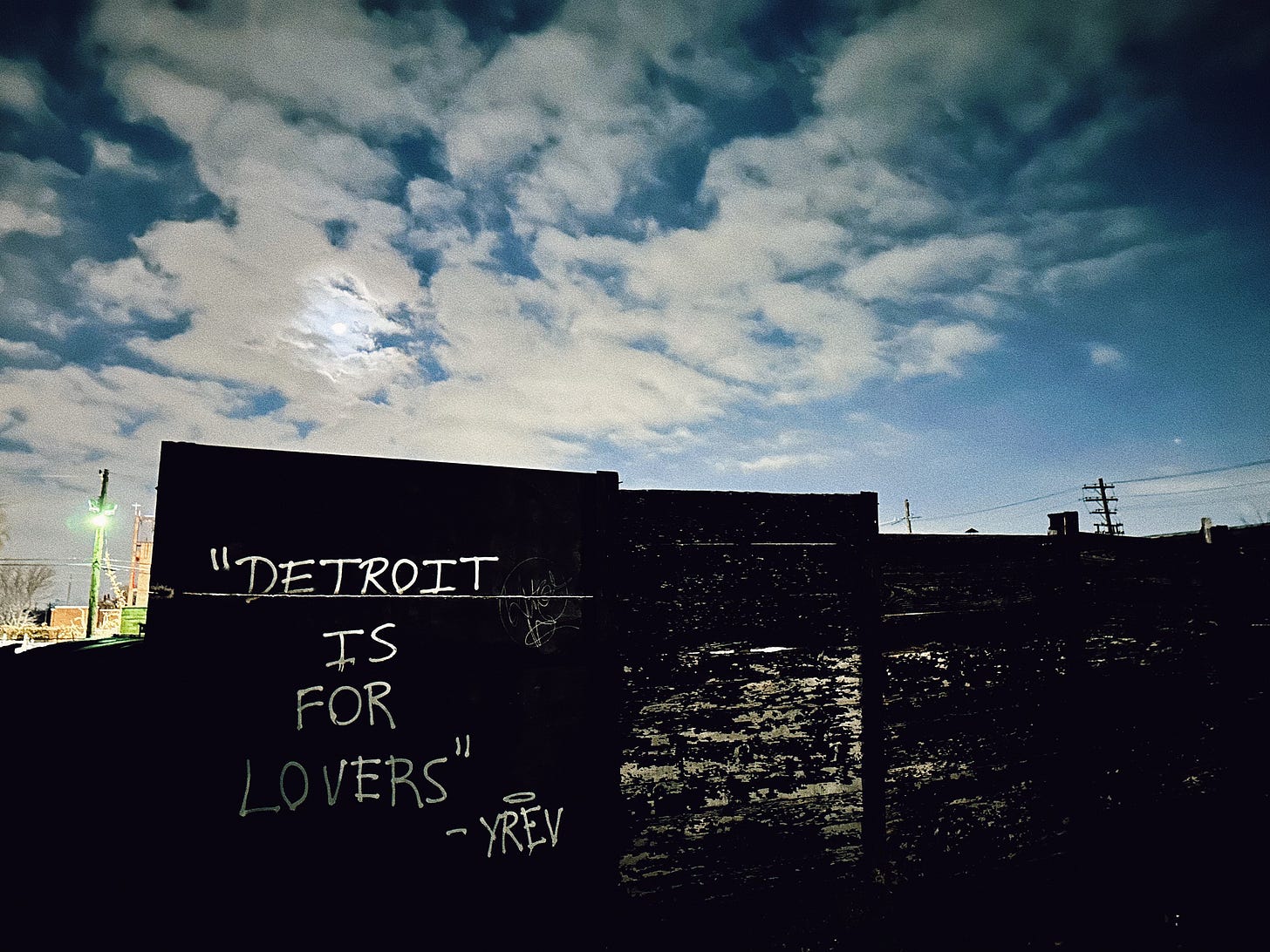 A mural at night, reading "Detroit is for Lovers - YREV"